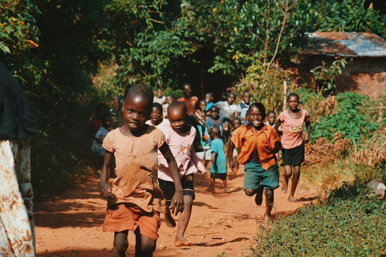 Children running along a dirt path between trees