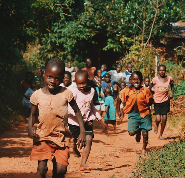 children running and walking on brown sand surrounded with trees during daytime