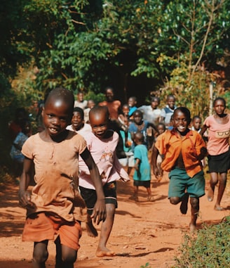 children running and walking on brown sand surrounded with trees during daytime