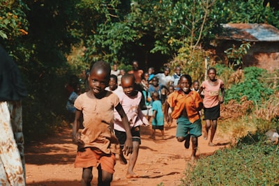 children running and walking on brown sand surrounded with trees during daytime charity teams background