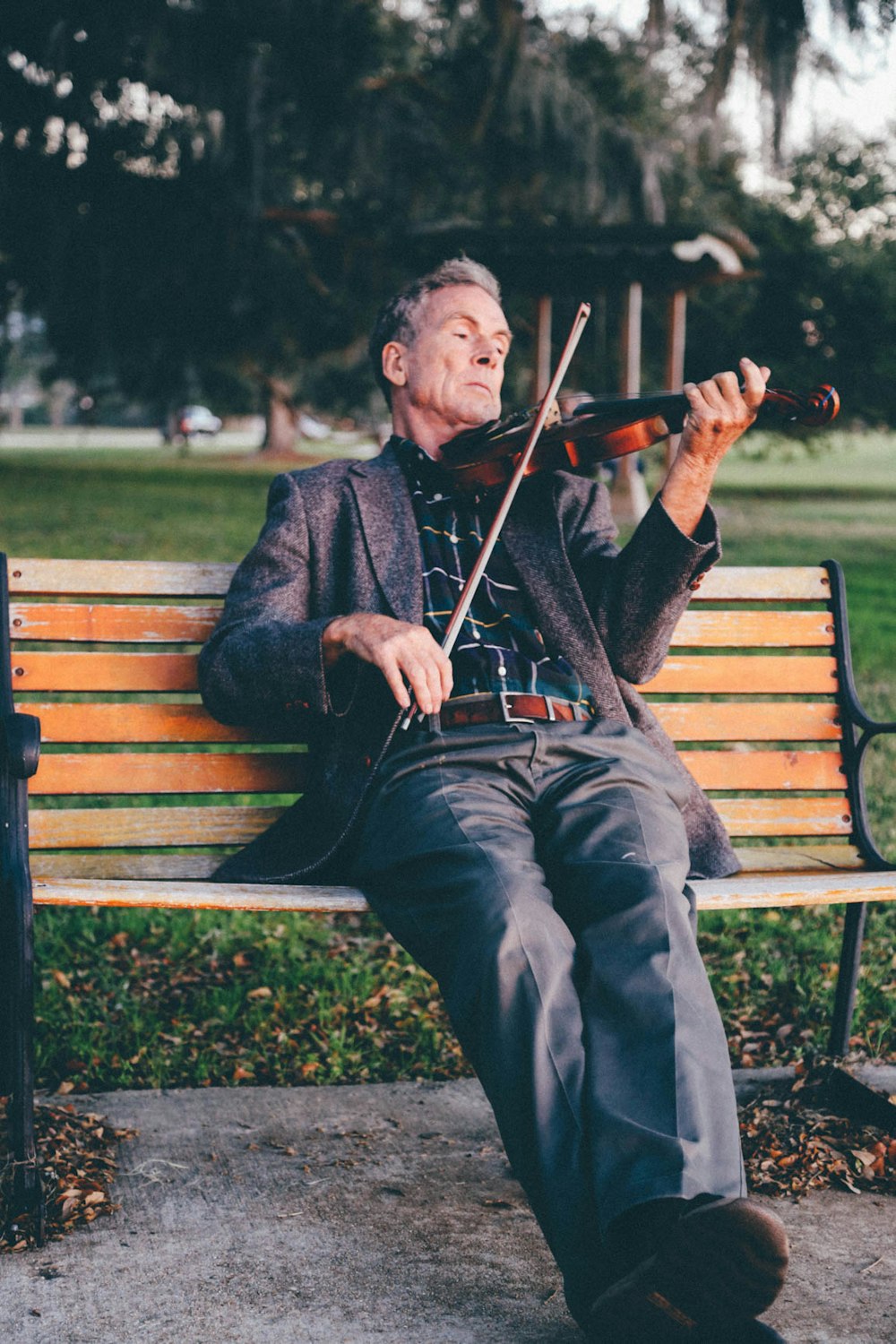 Un hombre mayor tocando un violín en un banco del parque.