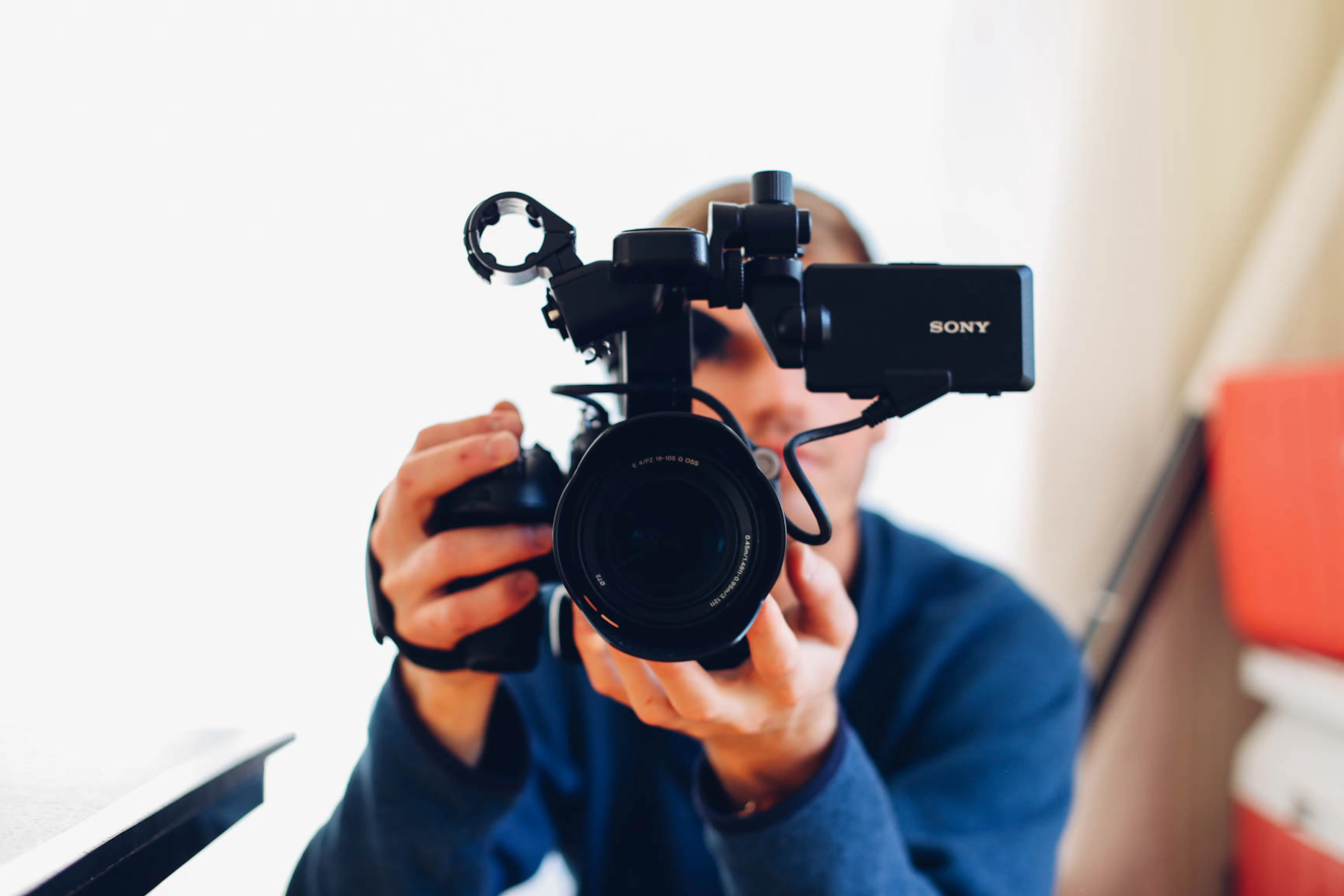 A videographer framing a shot with a cinema camera in a bright room