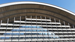 An architectural structure featuring a series of horizontal louvered panels arranged in an arc. The design allows for both functionality and aesthetics, with metallic elements and large glass windows reflecting the sky. The structure appears modern and utilitarian.