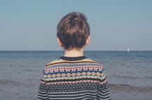 person wearing multicolored striped floral sweater facing the sea