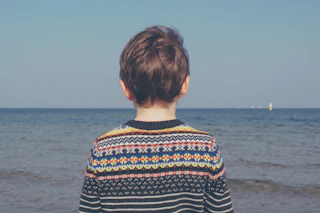 Child in a colourful fair isle jumper looking out to sea