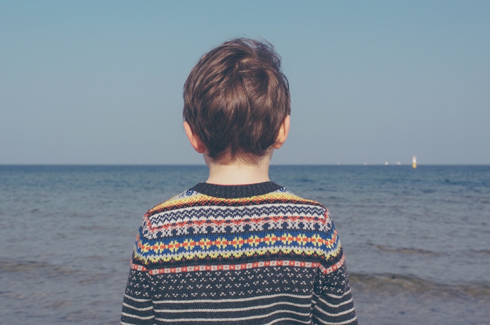 person wearing multicolored striped floral sweater facing the sea