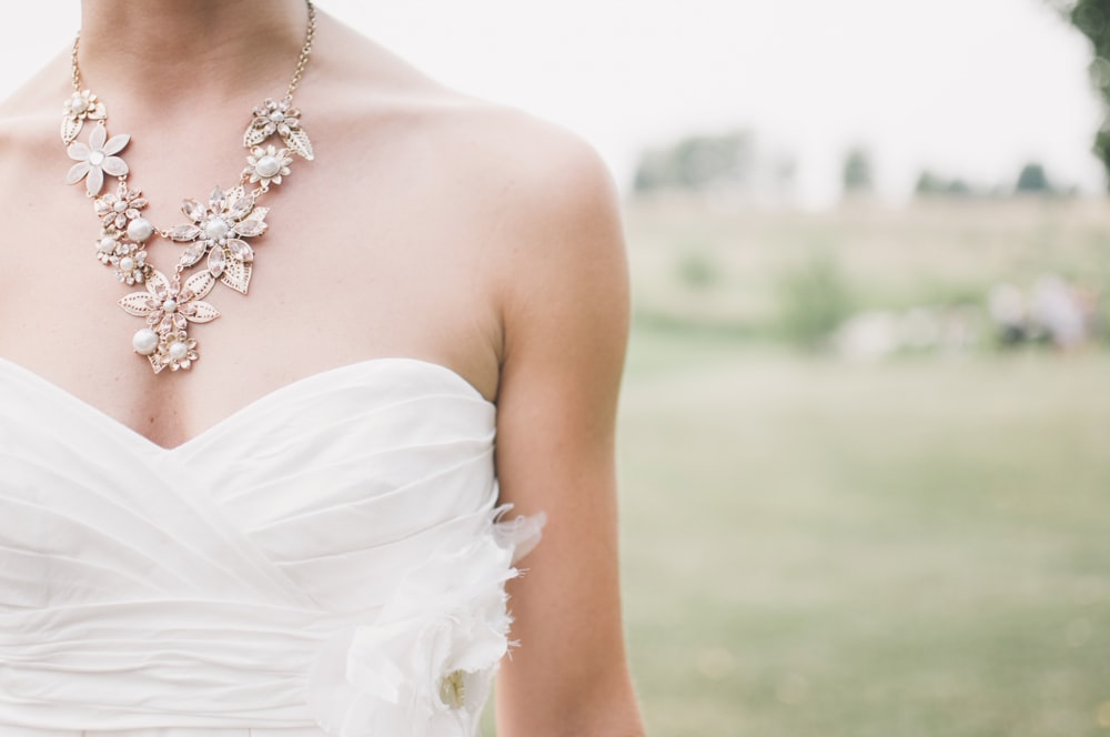 Bride wearing strapless dress and flower necklace stands in a grass field