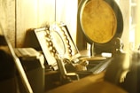 A collection of antique or vintage items arranged on a wooden shelf. Prominent objects include a decorative gold plate with intricate floral engravings, an ornate picture frame, and a small statuette of a person. The warm, golden hue lighting suggests a cozy, nostalgic atmosphere.