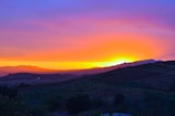 A vibrant landscape photograph showcasing a sunset over hills.