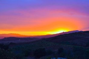 A vibrant sunset over rolling hills and fields.