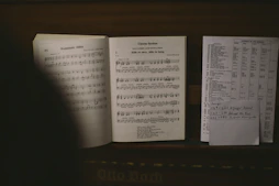 An open notebook with handwritten song lyrics beside a guitar on a wooden table