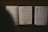 An open music book with visible musical notes and lyrics lies on top of a wooden surface. Next to it, there is a sheet of paper with text and a handwritten note listing song titles and numbers.