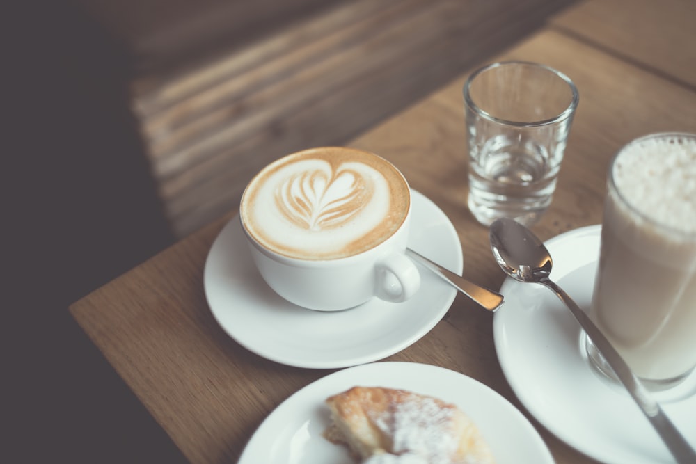 white cappuccino coffee near clear drinking glass