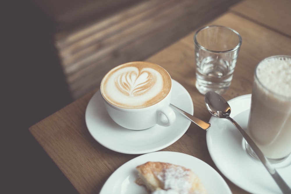Weißer Cappuccino-Kaffee in der Nähe von klarem Trinkglas