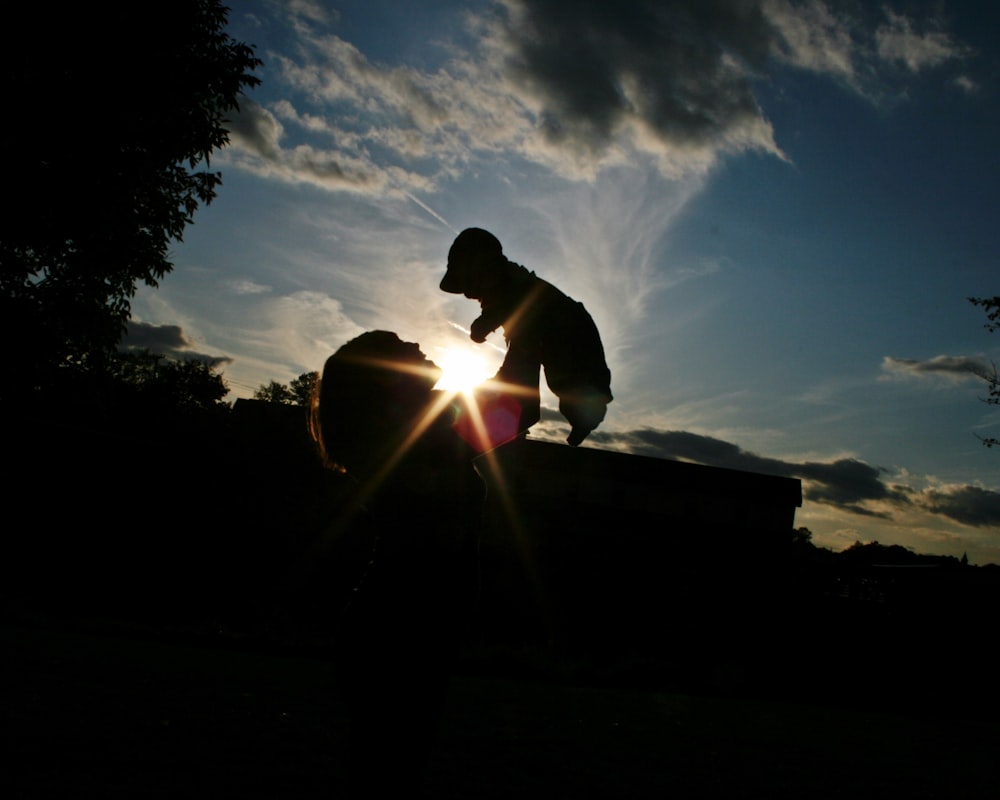 Parent lifts child up, as two are silhouetted against the sunlit sky