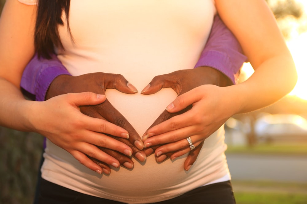 Man's hands wrap around the pregnant belly of his girlfriend