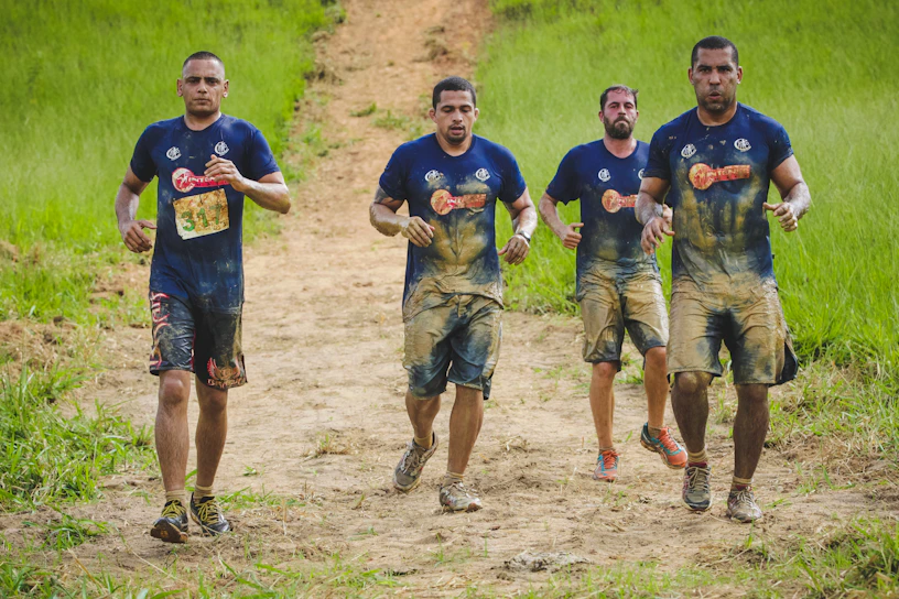 A group of competitors sprinting through a rugged outdoor course, dust flying around them.