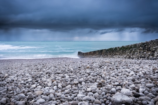 body of water across pebbles under dark sky in Étretat France