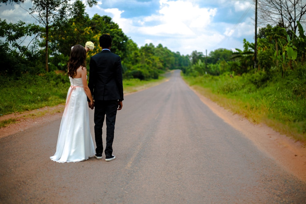 wedding couple standing on winding road between trees under cumulus cloud