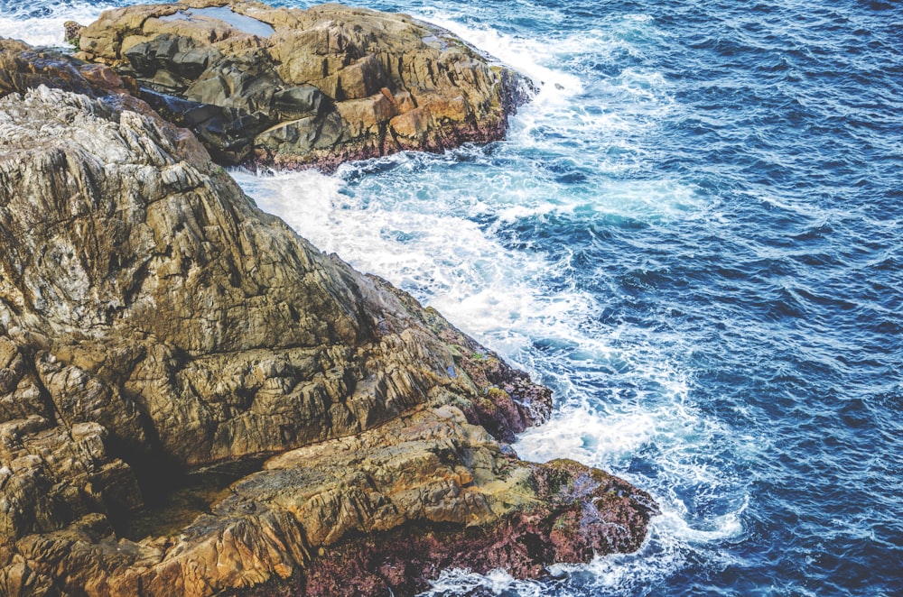 aerial photo of sea waves splashing through rocky mountain