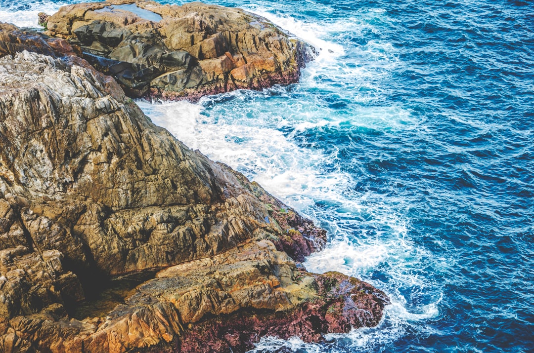 aerial photo of sea waves splashing through rocky mountain