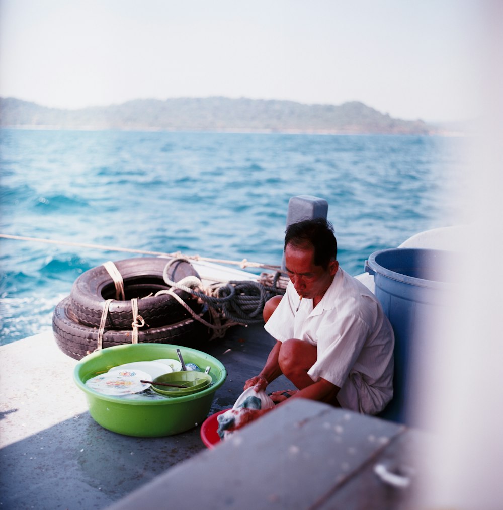 man washing dishes beside blue plastic pail