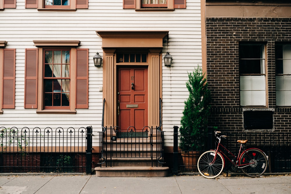 red bicycle parked beside black metal gate in front house