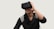 A person is using a virtual reality headset, appearing engaged and smiling. They are wearing a dark-colored sweater with light patterns on the shoulders and have long black hair.