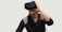 A person is using a virtual reality headset, appearing engaged and smiling. They are wearing a dark-colored sweater with light patterns on the shoulders and have long black hair.