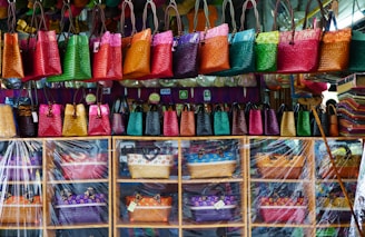 A vibrant display of colorful, custom-designed tote bags hanging in a sunny Indian artisan workshop.