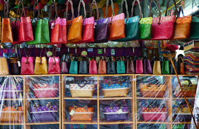 A vibrant display of handblock printed cotton bags hanging on rustic wooden hooks.