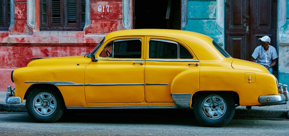 sedã amarelo estacionado perto de prédio de concreto vermelho