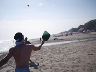A vibrant black-and-white photo of friends laughing and playing an outdoor paddle game on a sunny beach.