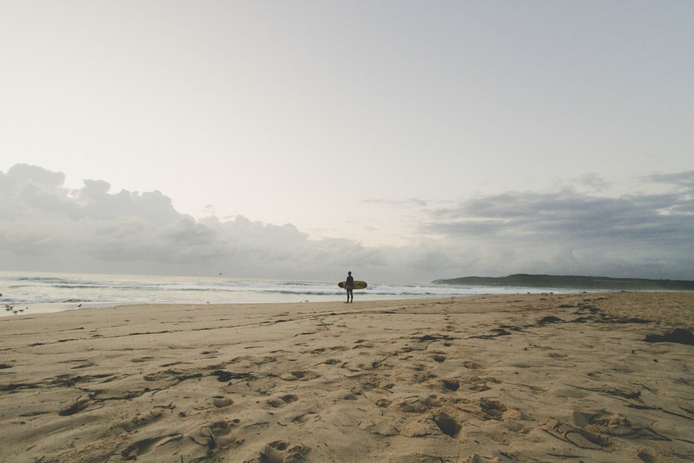 homem parado à beira-mar com prancha de surf
