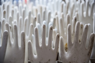 A collection of white rubber glove molds, with some of them showing signs of dirt or discoloration. The molds are arranged closely together, forming a repetitive pattern.