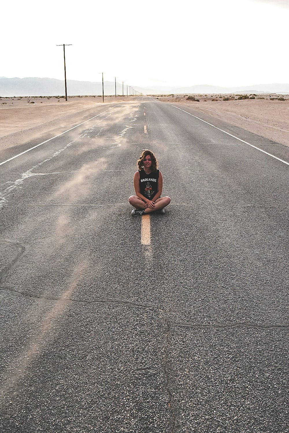 A girl sitting on yellow road line with her legs crossed.