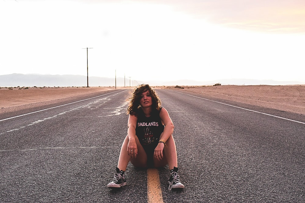 Una chica rockera sentada en la línea amarilla en medio de una carretera.