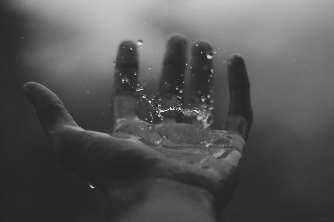 A black and white photo with a hand reaching out and rain falling on to it.