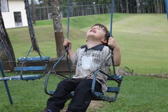 A child laughing joyfully on a playground swing under a bright blue sky.