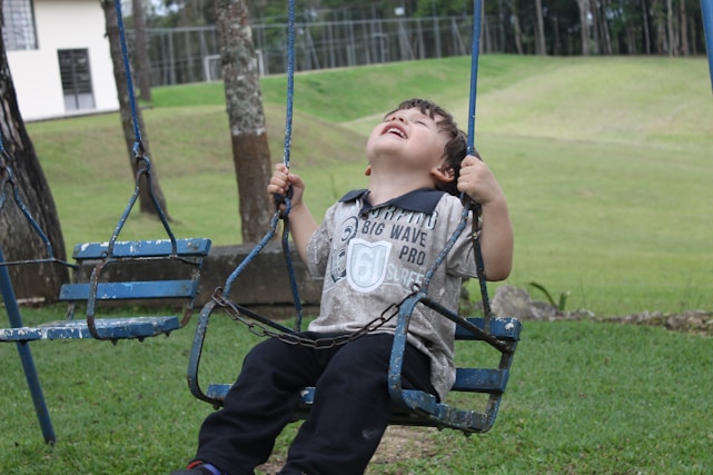 A child laughing joyfully on a playground swing under a bright blue sky.