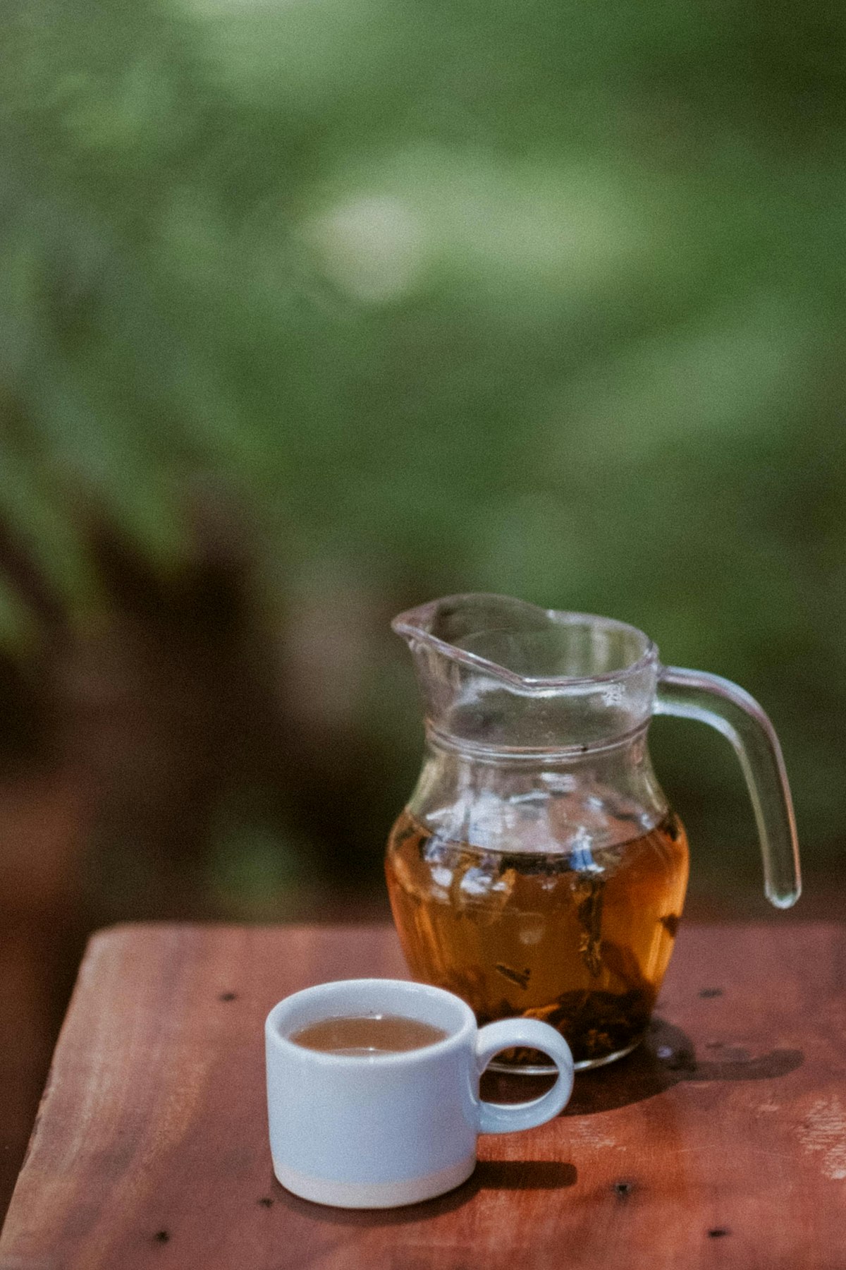 A clear glass pitcher of brewed tea with condensation, sitting on a wooden table