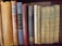 A collection of vintage and classic books of various sizes and colors are neatly lined up on a wooden shelf. The spines show titles such as 'Aristotle's Rhetoric and Poetics', 'Twelfth Night', and 'Poems by E.B. Browning'. The books vary in condition, indicating they are well-read and possibly valuable.
