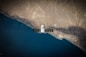 A satellite is positioned over a coastal landscape, highlighting a stark contrast between the deep blue ocean and the arid, brown rocky terrain. The satellite features a large solar panel array and is centered in the image, capturing both natural and technological elements.