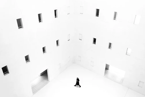 A dramatic black-and-white frame of a model walking through a minimalist, high-end interior.