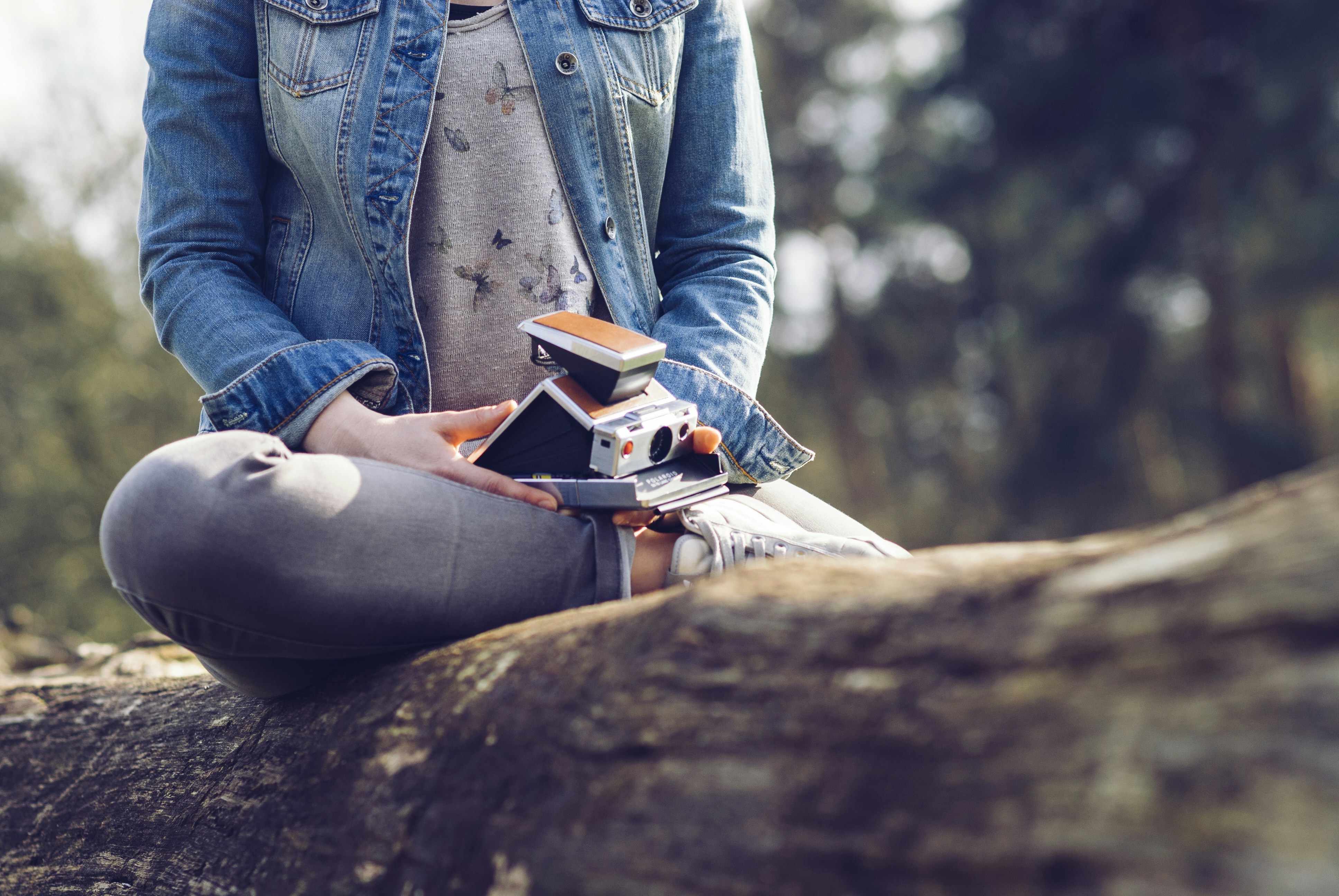 woman sitting on log holding camera and book