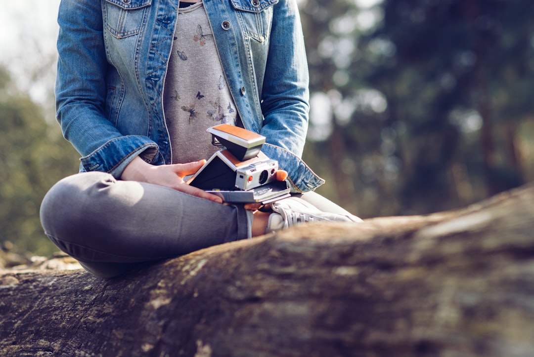 woman sitting on log holding camera and book