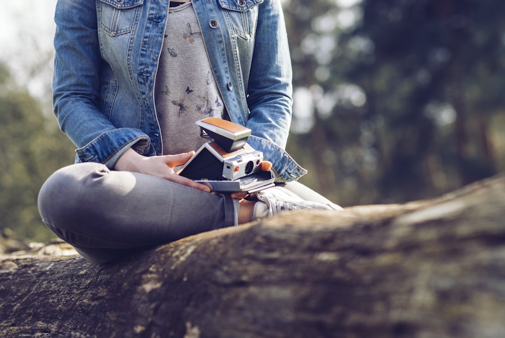 woman sitting on log holding camera and book