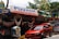 A souvenir and gift shop with a sign reading 'Playasol Souvenirs & Gift Shop', offering various items such as hanging hammocks and T-shirts. A bright red car is parked in front of the store. Colorful flags and greenery surround the shop.