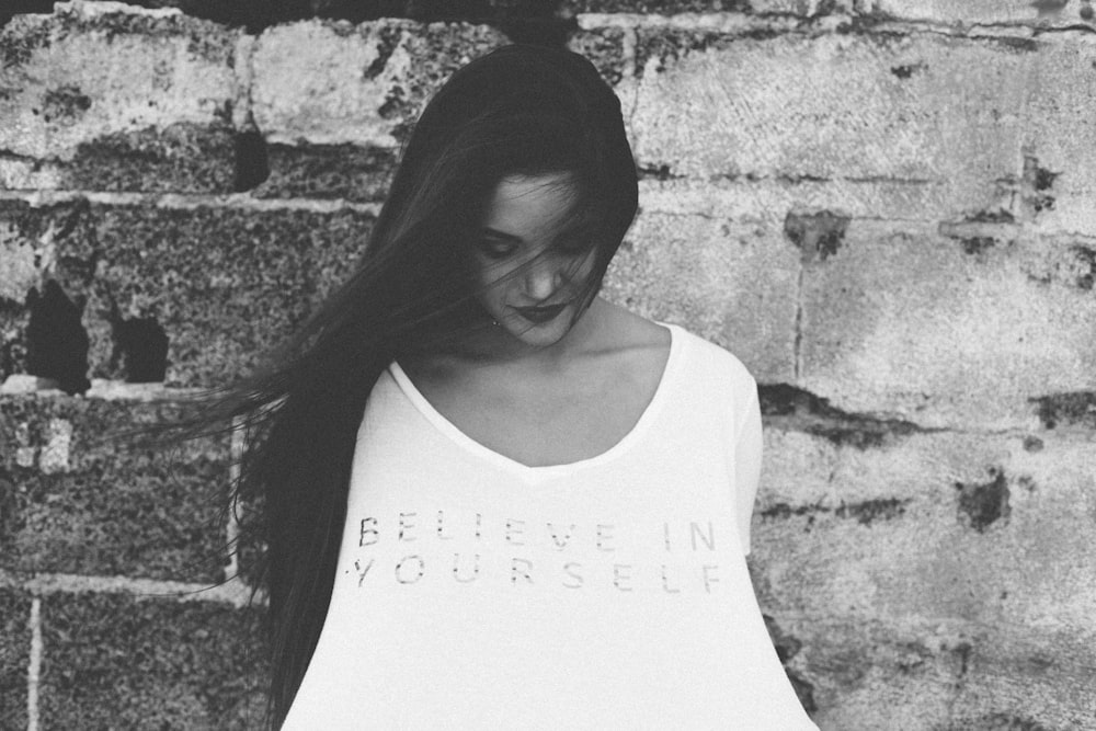 A woman looking down at her shirt which reads "Believe in yourself."