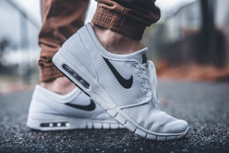 person wearing white Nike running shoes standing on black concrete path